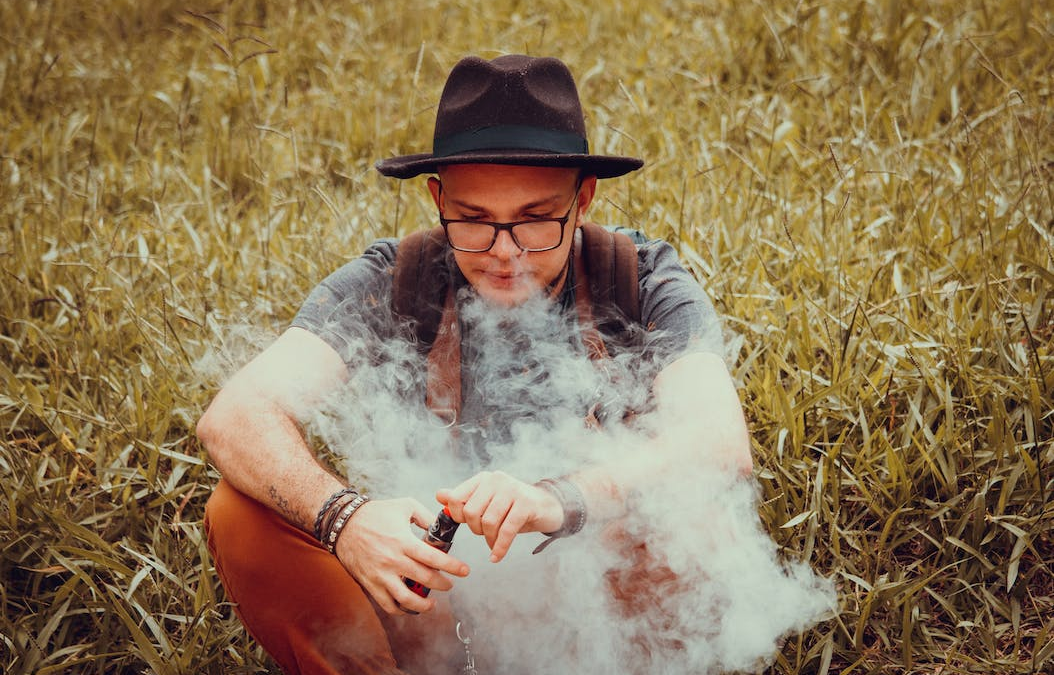 A person sitting on the grass and vaping